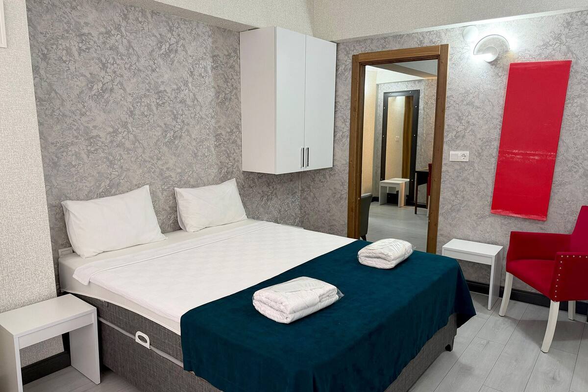A bedroom with a bed, a white wardrobe, a mirror, a red chair, and a small table.