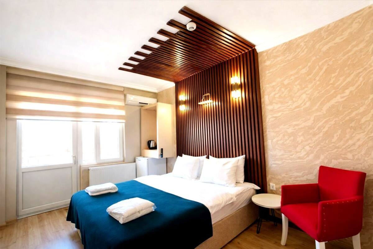A modern hotel room with a bed, a red armchair, and a small table.