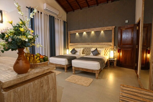 A bedroom with two beds, a wooden headboard, a bedside table with a lamp, and a vase with flowers on a wooden dresser.