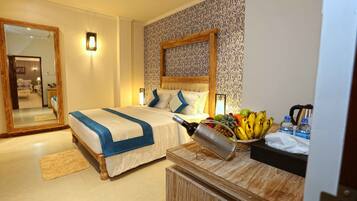 A hotel room with a large bed, a wooden headboard, a bedside table with a fruit basket, and a mirror.