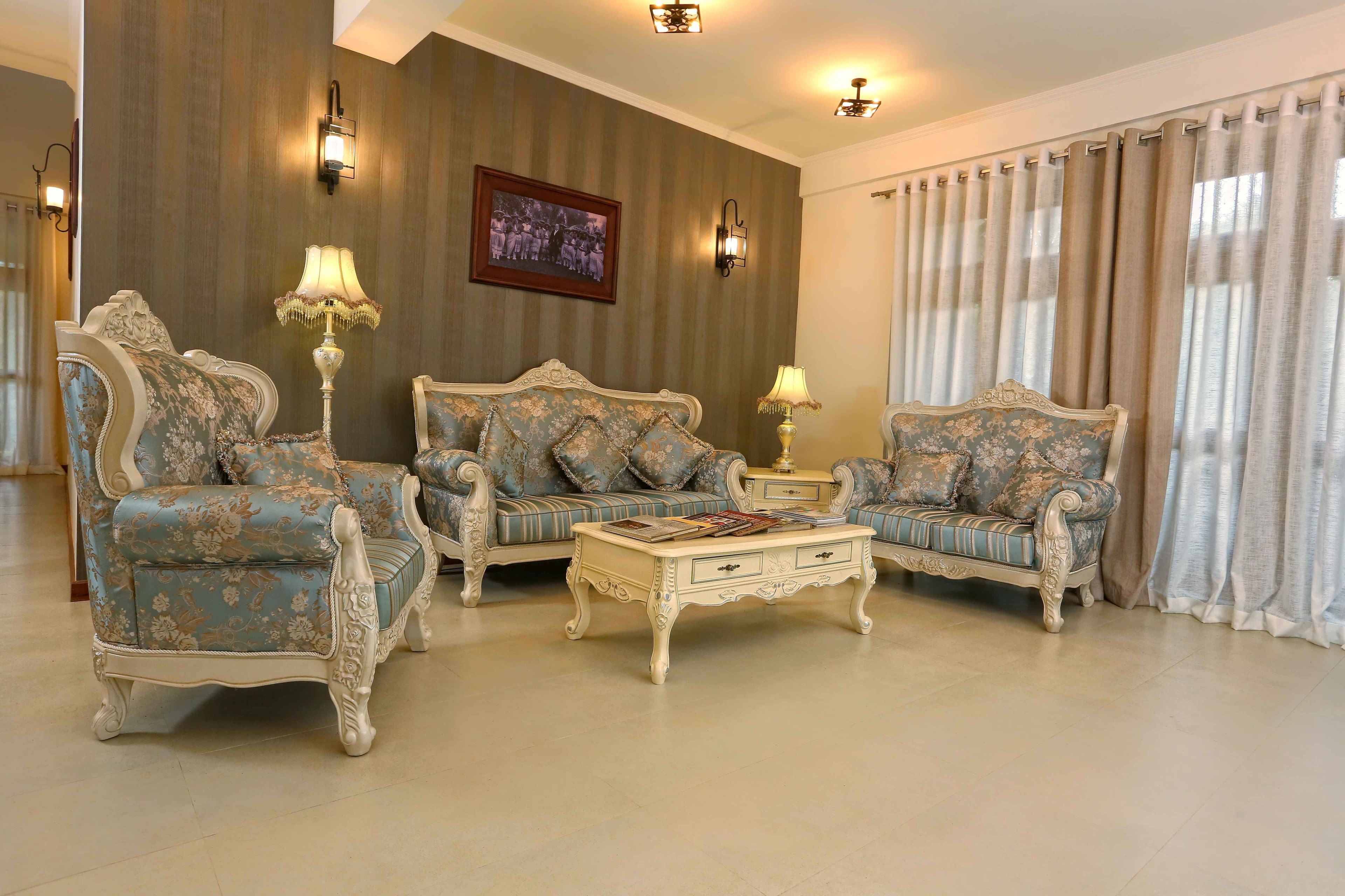 A living room with ornate furniture, including two sofas and a coffee table, with wall-mounted lamps and a framed picture on the wall.