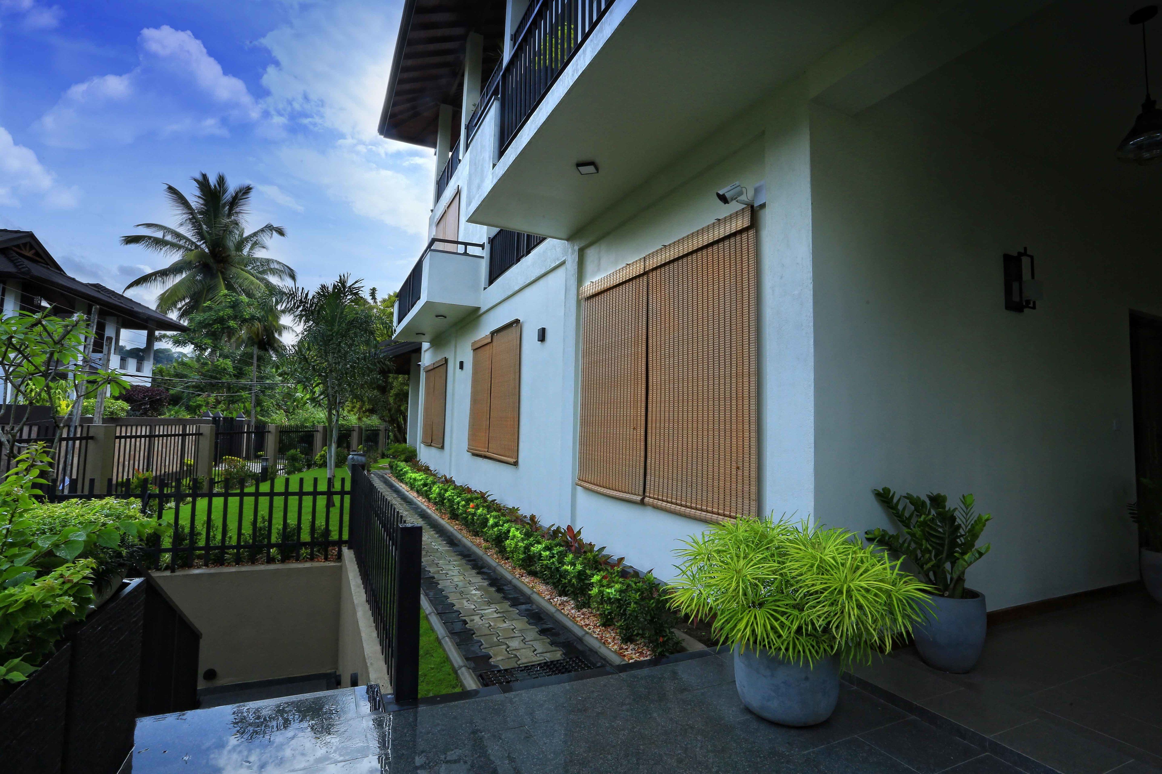 A modern residential building with a covered balcony, a small garden with a pathway, and potted plants.