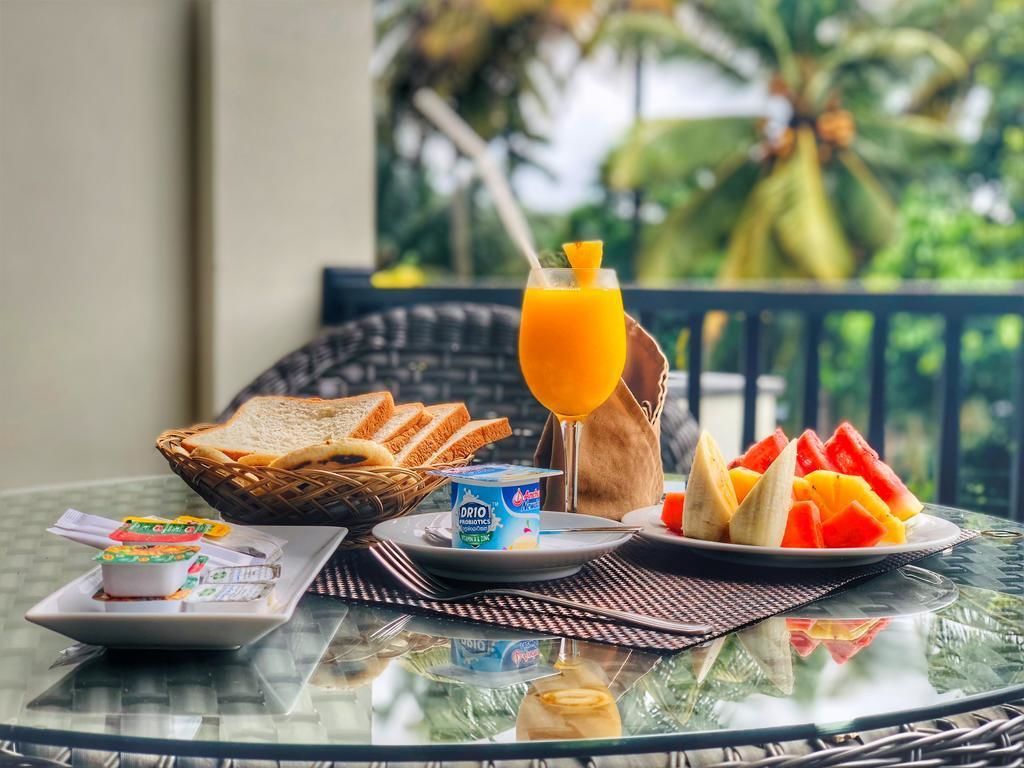 A breakfast setting with toast, yogurt, fruit, and orange juice on a glass table with a view of palm trees.