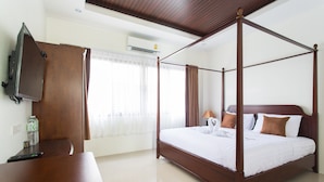 A four-poster bed with white bedding, a wooden desk with a remote control, and a television on the wall.