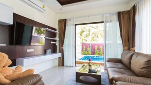 A modern living room with a flat-screen TV, a sofa, a coffee table, and a view of a swimming pool.