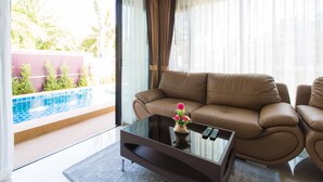 A modern living room with a brown leather sofa, a glass coffee table with a vase of flowers, and a view of a swimming pool through large windows.
