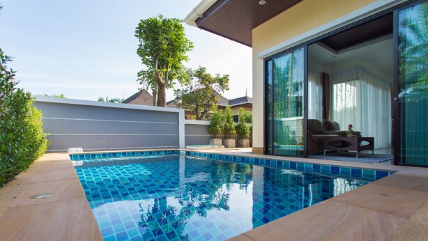 A swimming pool with tiled edges, a wooden deck, and a glass door leading to a covered outdoor area.
