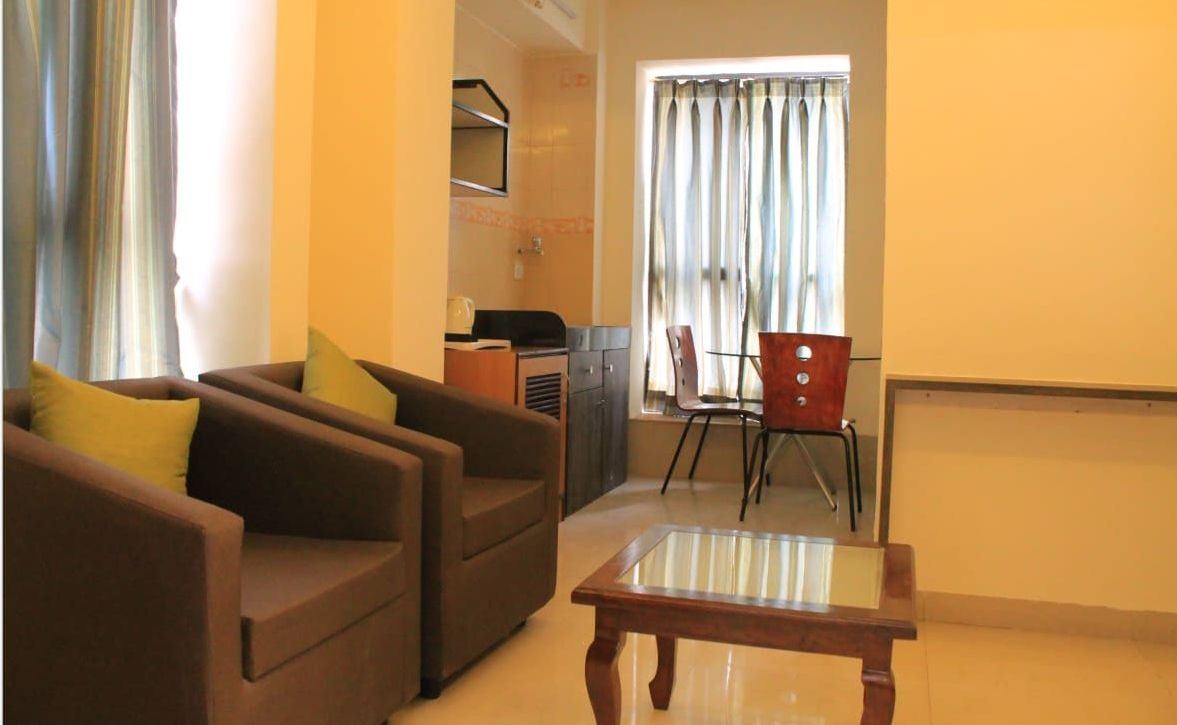A living room with a sofa set, a glass-top coffee table, a dining table with chairs, and a kitchen area in the background.