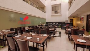 Ein Hotelrestaurant mit mehreren Tischen und Stühlen, einem Küchenbereich im Hintergrund und einem Schild mit dem Logo und dem Namen des Hotels.