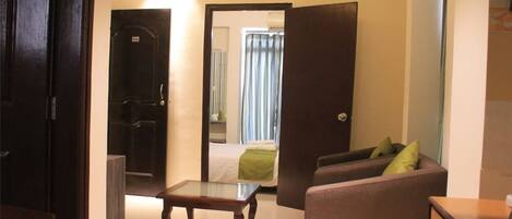 A hotel room with a bed, a sofa, a small table, and a door leading to a bathroom.
