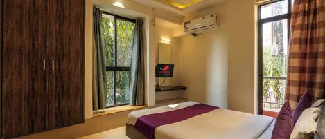A bedroom with a bed, a wardrobe, a window with curtains, an air conditioning unit, and a mirror.