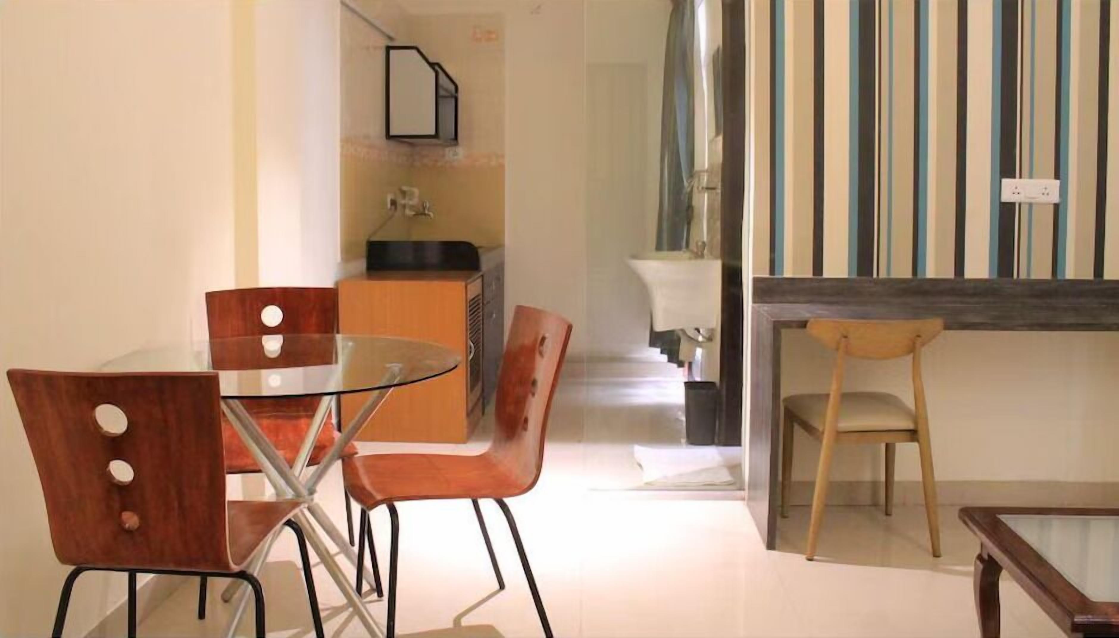 Un comedor con una mesa de vidrio y sillas de madera, una kitchenette al fondo y una cortina a rayas.