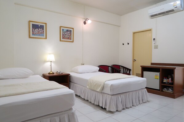A hotel room with two beds, a bedside table with a lamp, a small refrigerator, and a wall-mounted air conditioner.