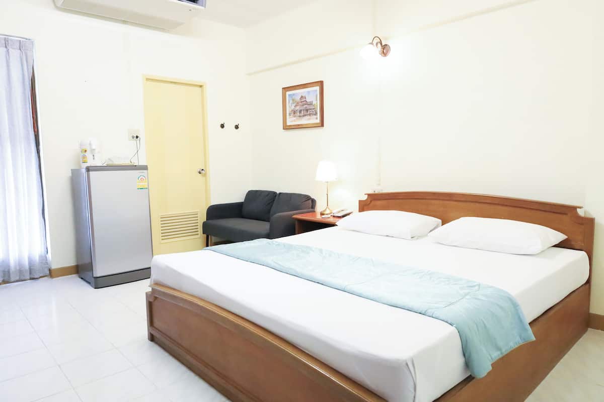 Quarto de hotel com cama, escrivaninha, cadeira, frigorífico e porta.