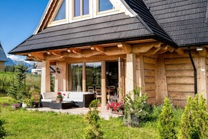 A wooden house with a sloped roof, a covered porch, and a glass door leading to an interior space.