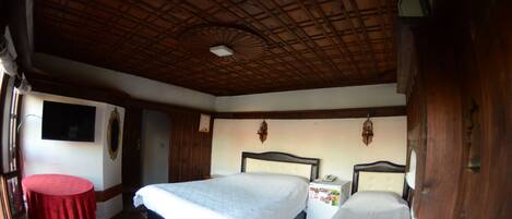 A room with two beds, a small table, and a wooden ceiling.