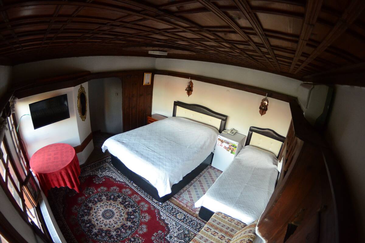 Een slaapkamer met twee bedden, een rode tafel, een televisie en een kamerkleed met een patroon.