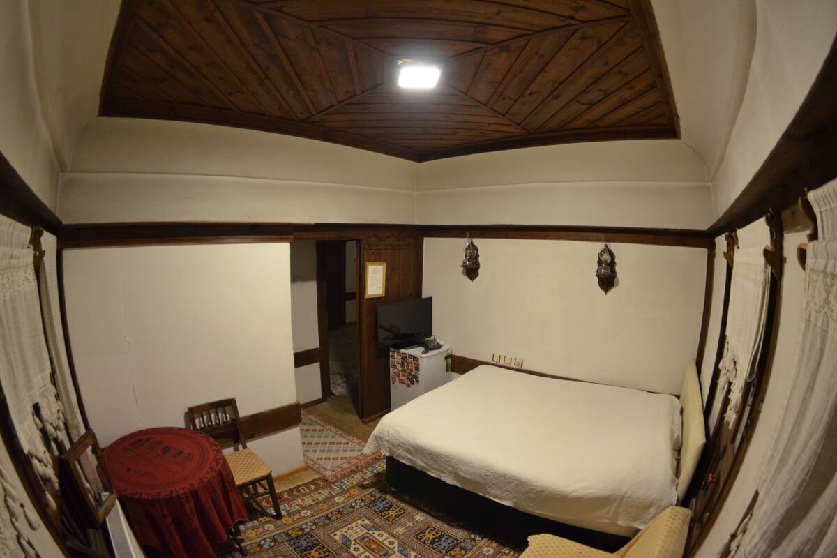 Een slaapkamer met een houten plafond, een bed, een klein tafeltje en een stoel.