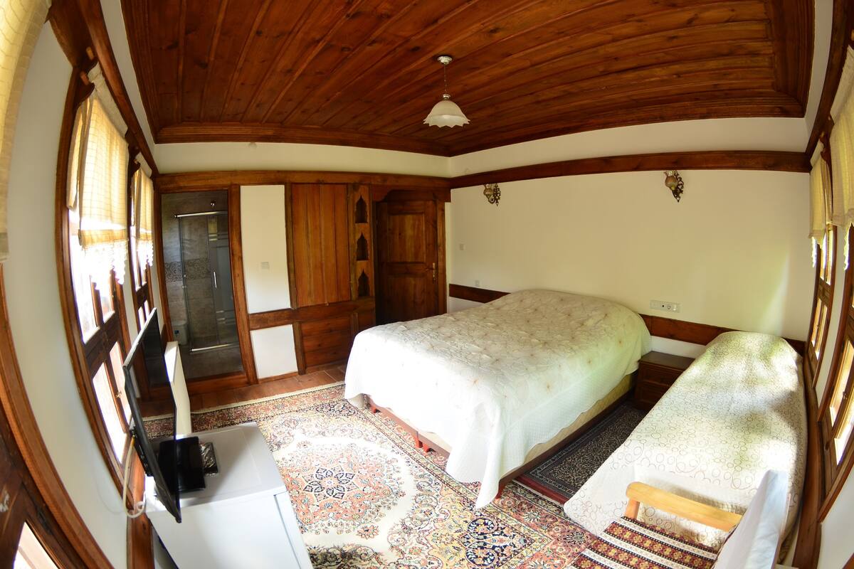 Een slaapkamer met een groot bed, houten plafond en een klein bureau met stoel.