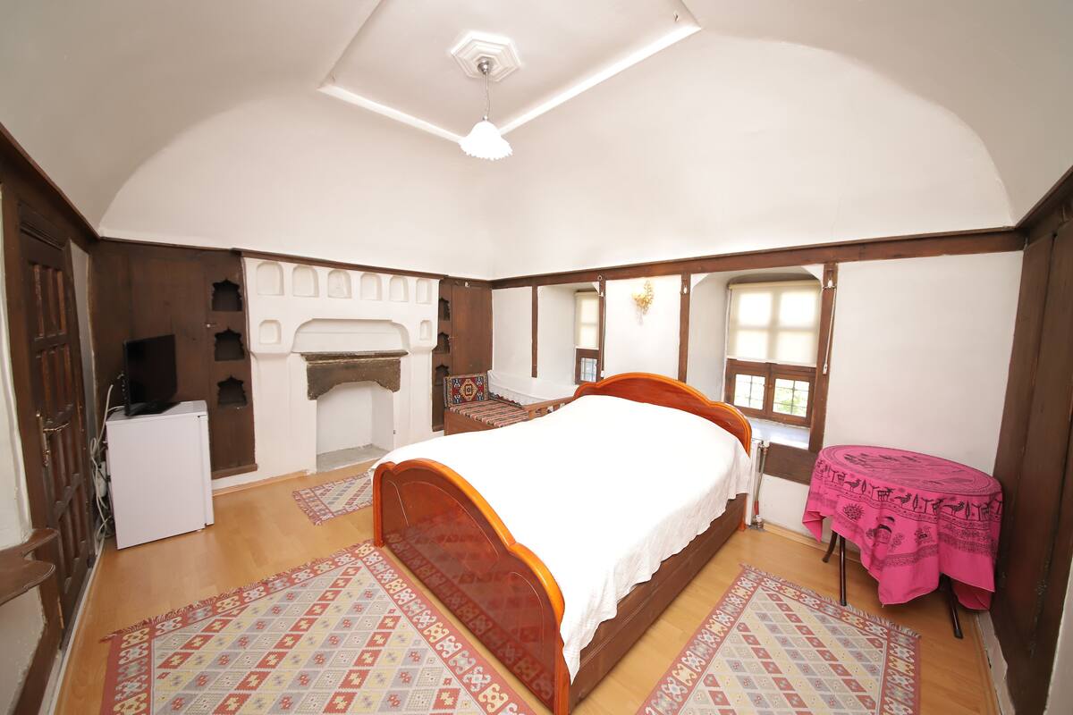 Een slaapkamer met een houten bed, een klein tafeltje met een roze tafelkleed en een open haard.