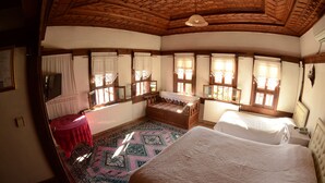Een klassieke kamer met houten plafond, een kamerbreed tapijt met dessin, twee bedden, een klein tafeltje en een raam met uitzicht.
