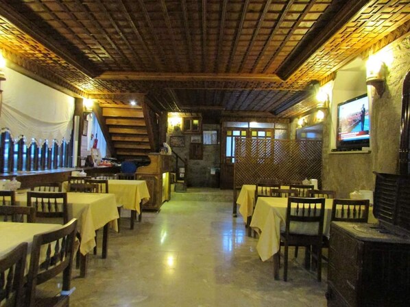A restaurant with wooden tables and chairs, a brick ceiling, and a staircase leading to an upper level.