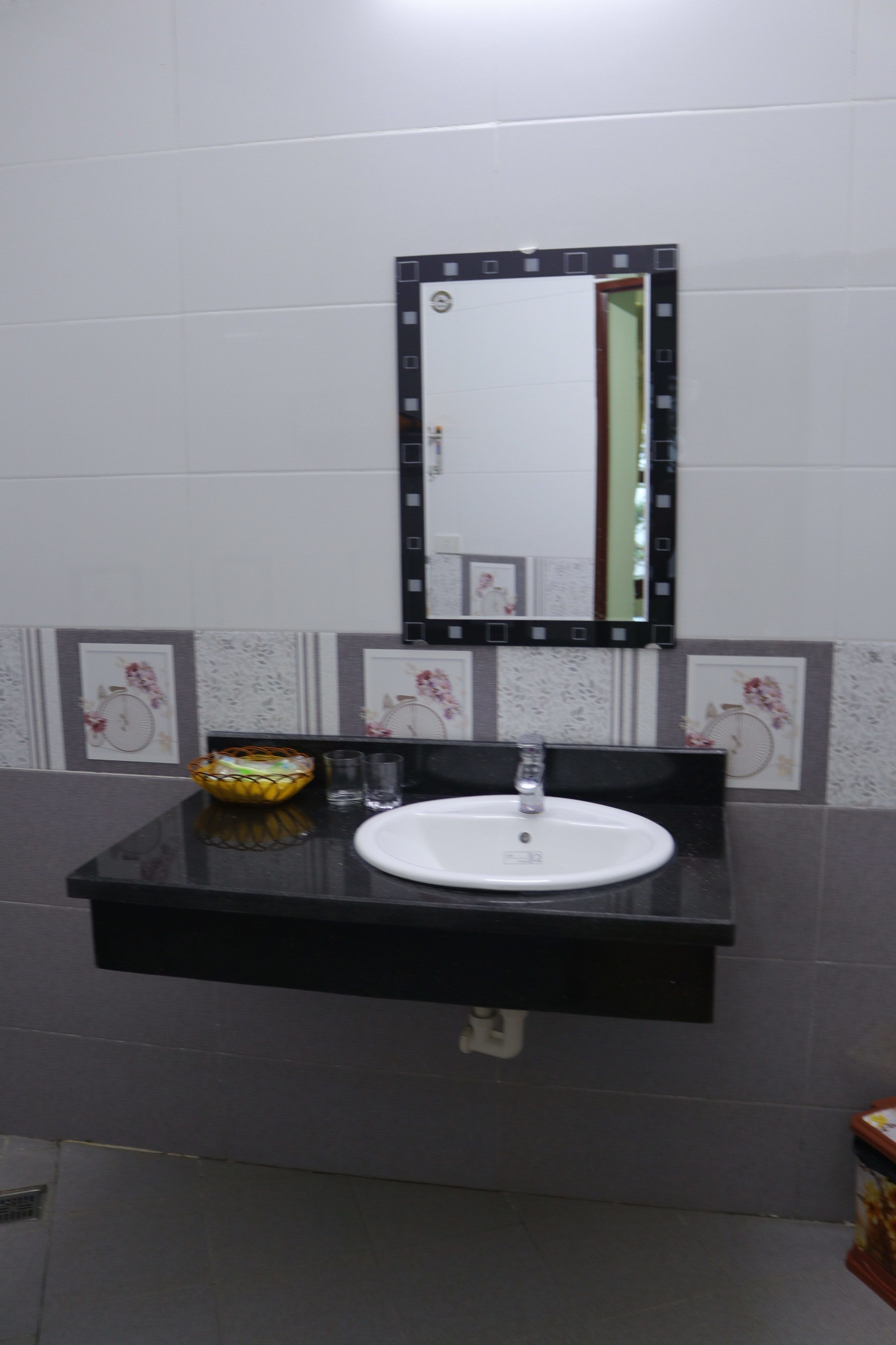 A bathroom with a white sink, black countertop, and a mirror with a black frame.