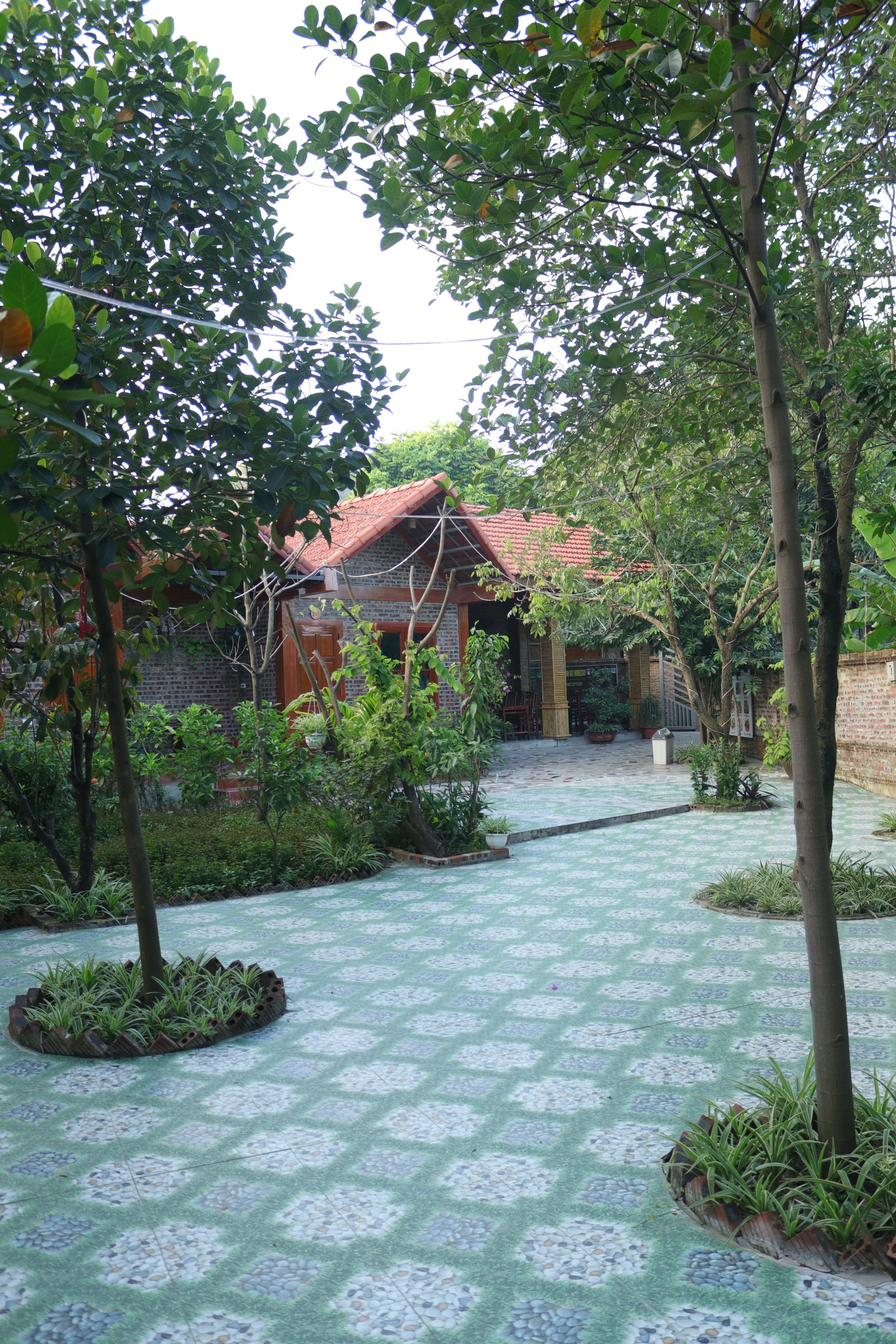 A courtyard with a patterned floor, surrounded by trees and a building with a red roof.