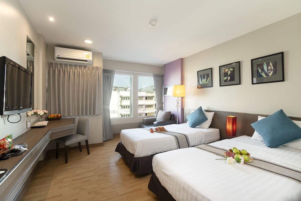 A hotel room with two beds, a desk, a TV, and a window with curtains.