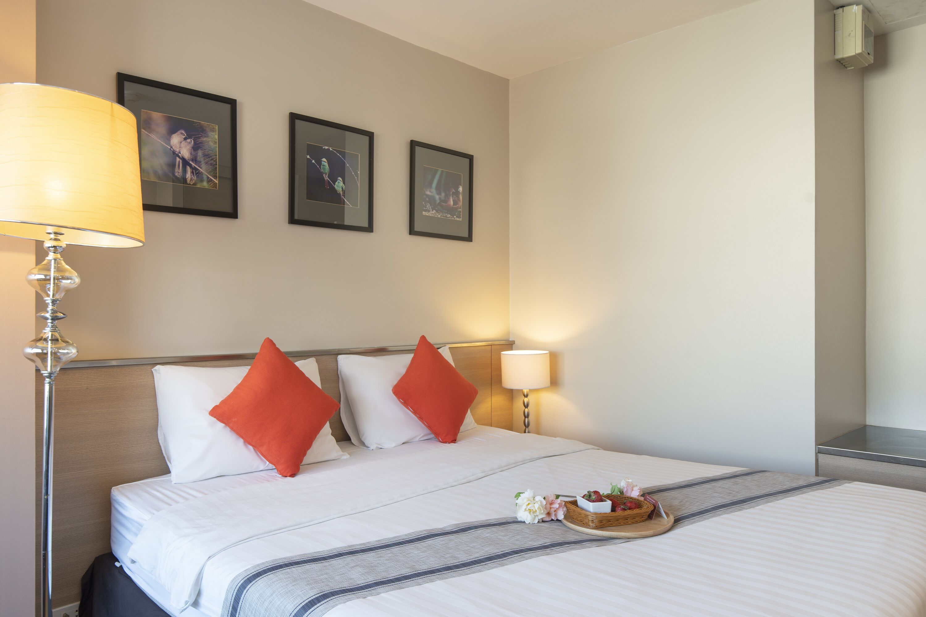 Habitación de hotel con cama, dos almohadas, mesita de noche con lámpara y bandeja con flores.