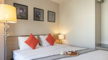 Een hotelkamer met een bed, twee kussens, een nachtkastje met een lamp en een dienblad met bloemen.