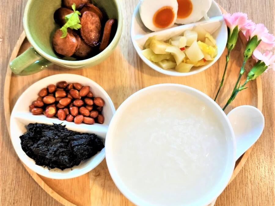 A wooden tray with various food items including a bowl of rice, a bowl of peanuts, a bowl of black fungus, a bowl of sliced sausages, a bowl of sliced boiled eggs, and a bowl of sliced potatoes.