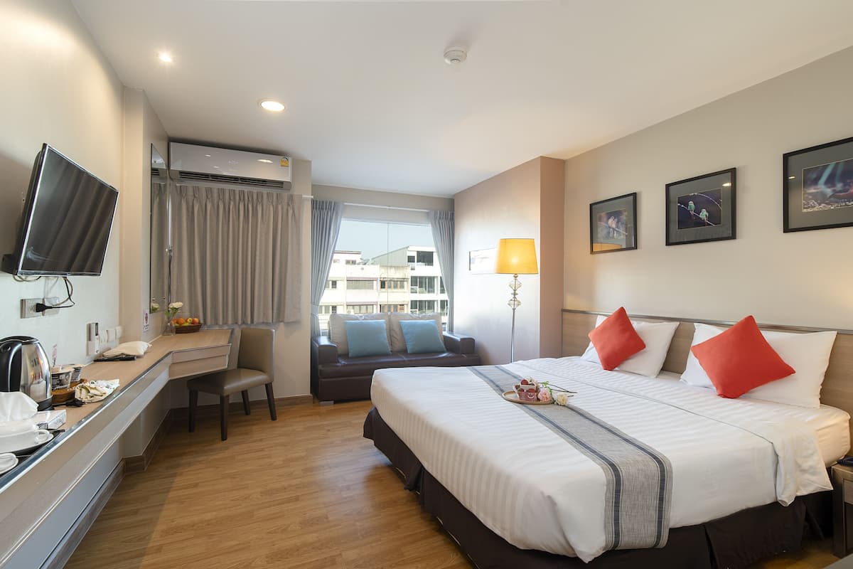 A hotel room with a bed, a desk, a TV, a window with curtains, and a lamp.