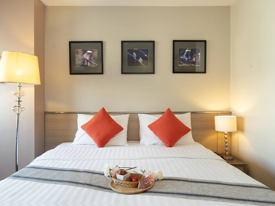 Una habitación de hotel con una cama bien hecha, una mesita de noche con una lámpara y tres cuadros en la pared.