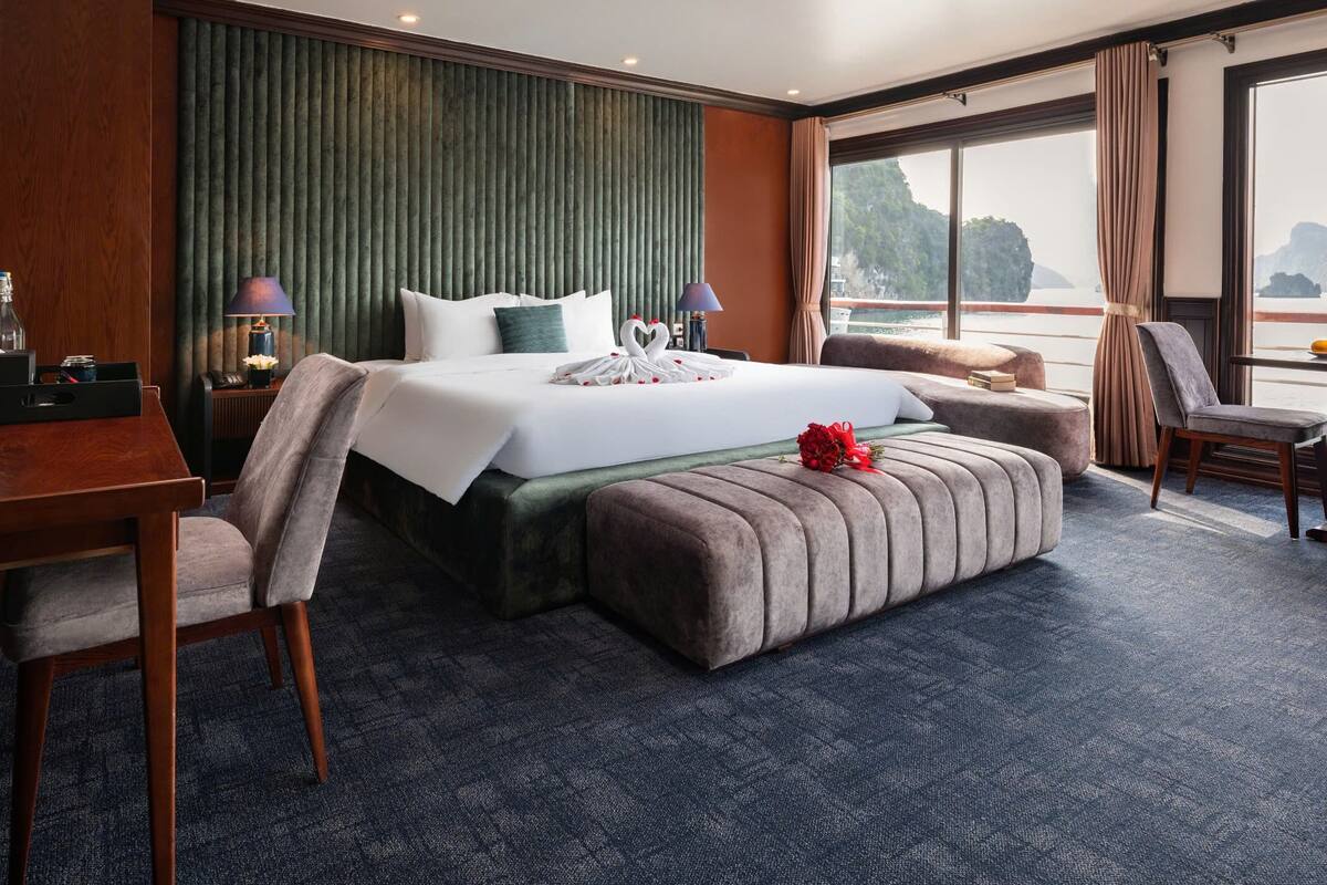 A hotel room with a large bed, a desk, a chair, and a view of the sea.