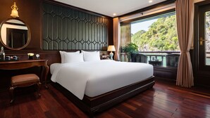 A large bed with a dark headboard, a bedside table with a lamp, a chair, and a view of a balcony with plants. - Rosa Boutique Cruise (Tuan Chau)