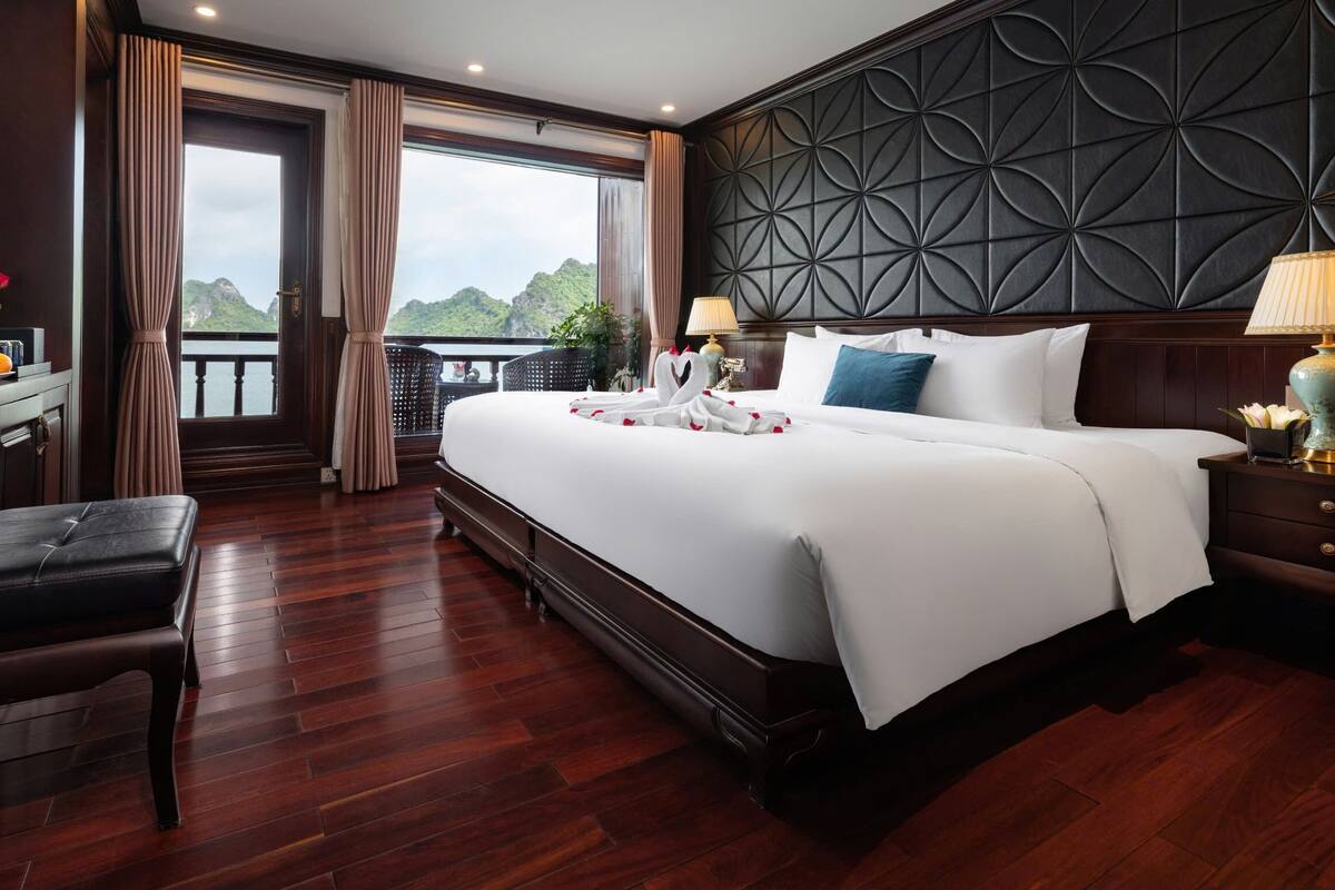 A hotel room with a large bed, a desk, a chair, a TV, and a balcony with a view of the mountains.