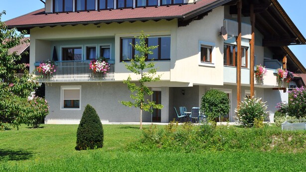 A two-story house with a balcony, a small garden, and a clear blue sky. - Karglhof - Villa (Finkenstein am Faaker See)