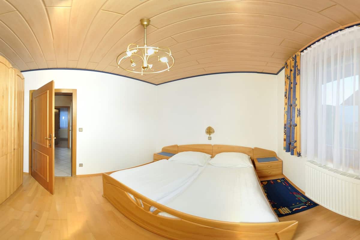 A bedroom with a wooden bed, a chandelier, a window with curtains, and a door leading to another room.