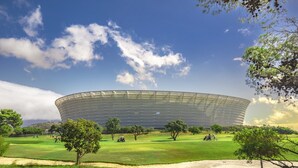 Un estadio grande y circular con techo transparente, rodeado por un campo cubierto de césped y árboles.
