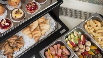Een buffet met diverse gerechten, waaronder gebak, fruit, groenten en vlees.