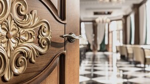 Uma porta de madeira com esculturas elaboradas e um interior moderno com piso xadrez e um candelabro.