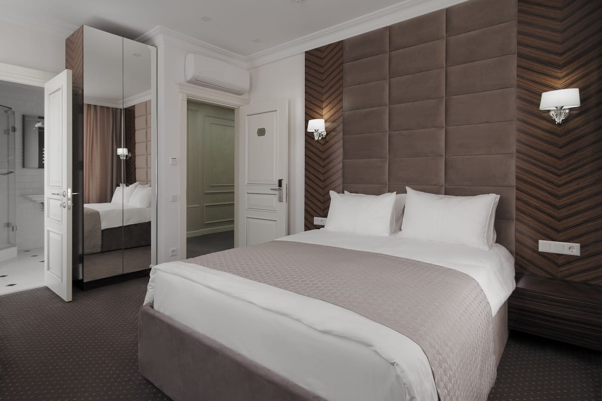 A hotel room with a large bed, a wardrobe, a mirror, and a wall-mounted light fixture.