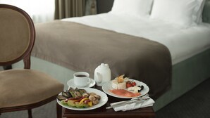 Cama bem arrumada com lençóis brancos, mesa de cabeceira com chaleira, pratos de comida e uma xícara de café.