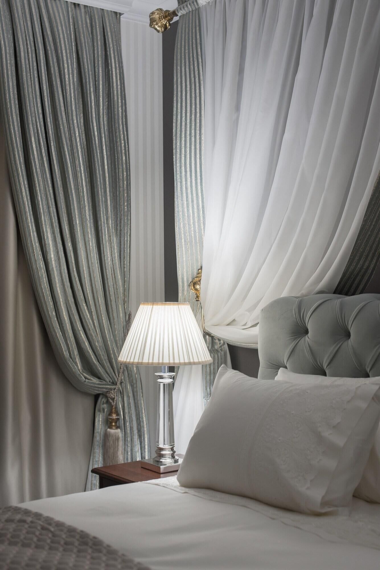 Quarto com cama, luminária e cortinas.