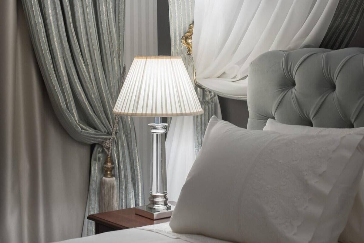 Quarto com cama, luminária e cortinas.