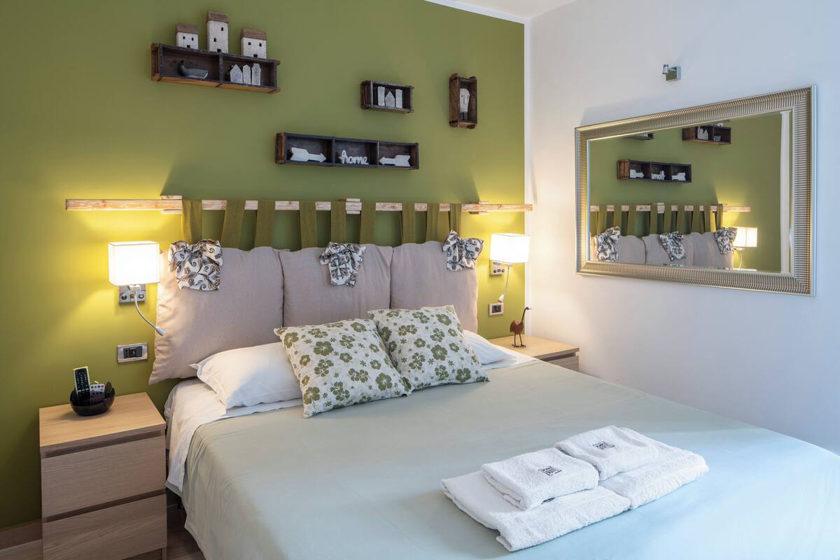 A neatly made bed with floral pillows, a bedside lamp, and a nightstand with a remote control.