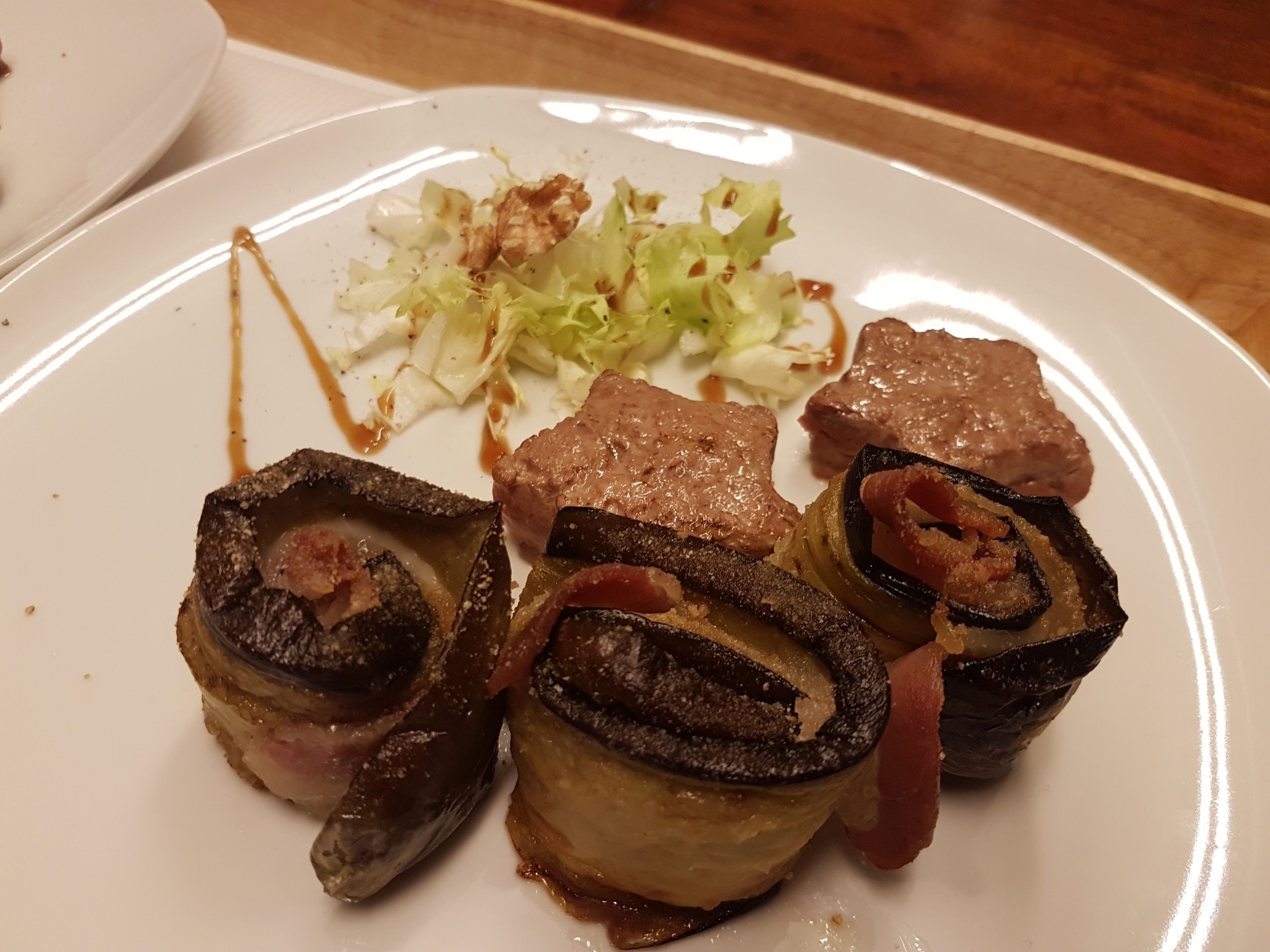 Un plato con carne enrollada y verduras, posiblemente un tipo de rollo o plato relleno, acompañado de col rallada y una pequeña cantidad de salsa.