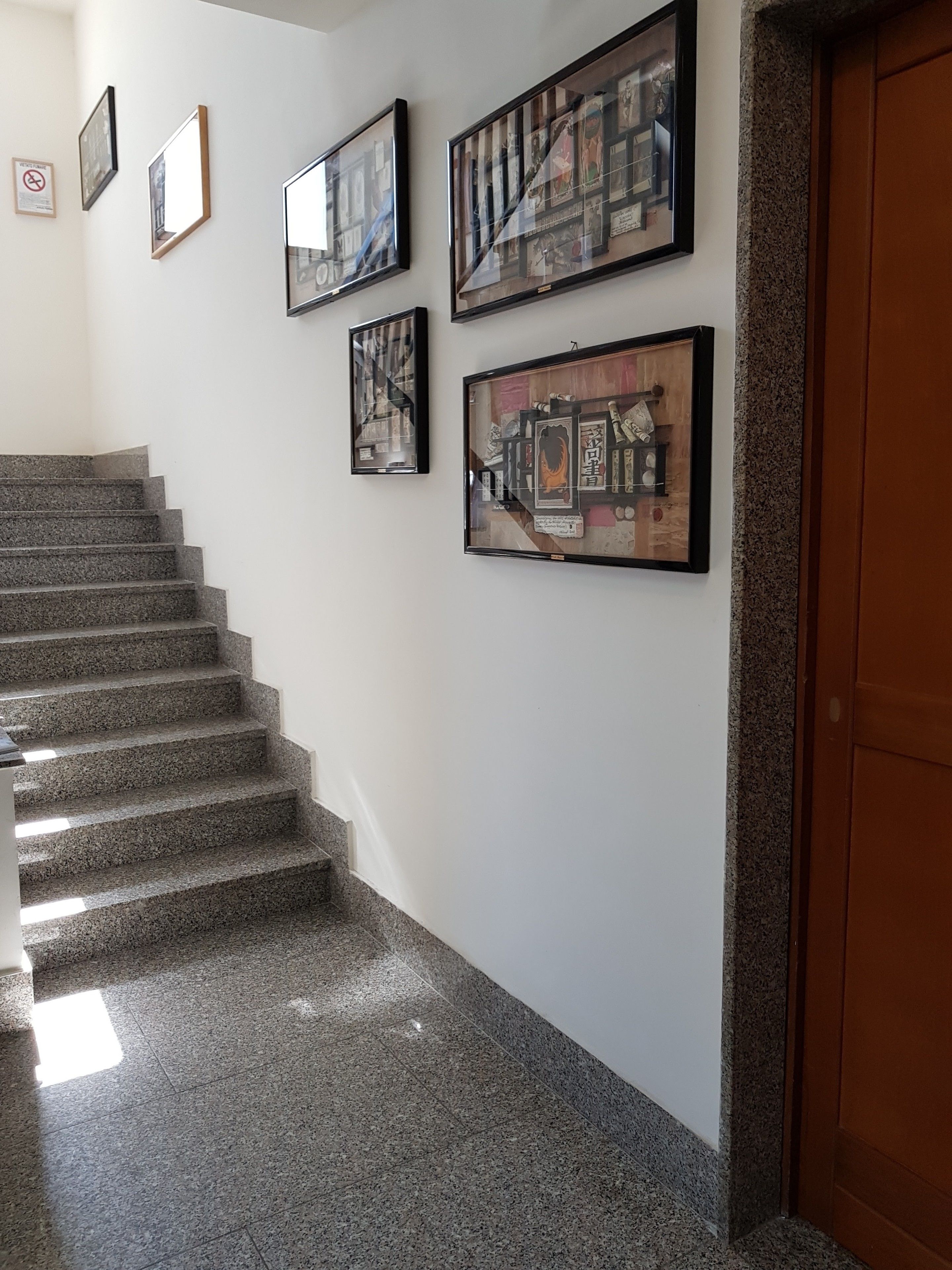 A staircase with granite steps leading to a landing where four framed artworks are displayed on the wall.