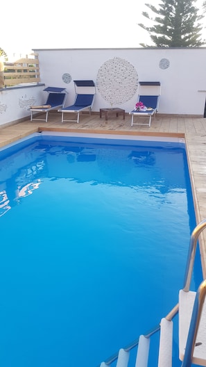 Una piscina al aire libre de temporada, tumbonas